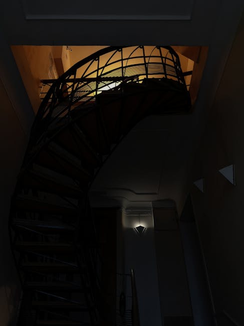 Inside a residential property, a curved metal staircase with black railings and wooden treads ascending from the ground floor to an upper level, visible through an opening in the ceiling. The staircas